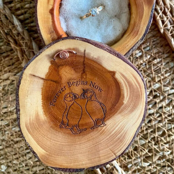 Yew wood ring box with 2 puffins engraved on it's lid. Written above the birds it says Forever Begins Now.
