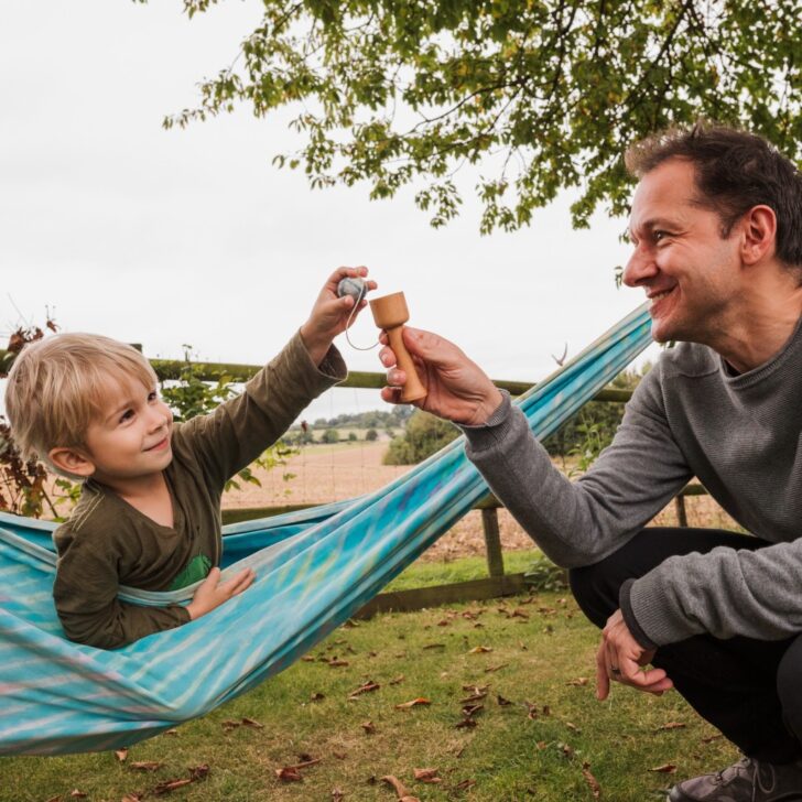 father and son playing with a wooden cup and ball game outdoors.