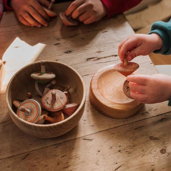 children's hands playing with wooden spinning tops
