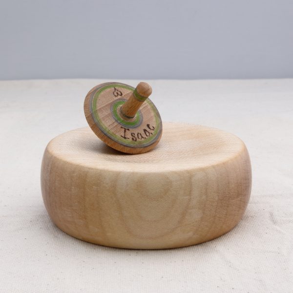 a personalised green and blue wooden spinnig top on a wooden base