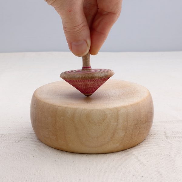 a wooden spinning top being held on a wooden base abou to be spun