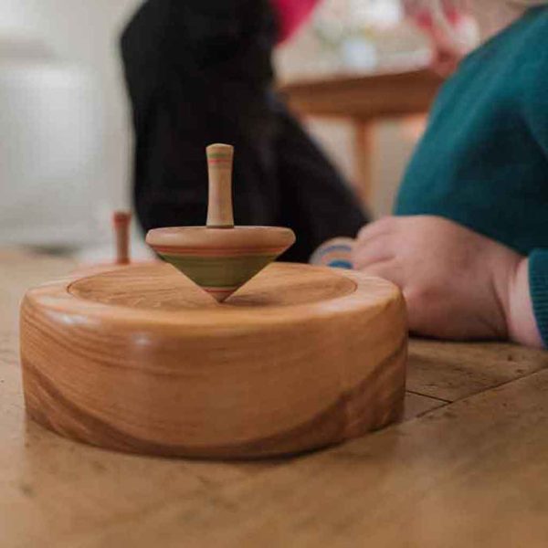green and pink wooden spinning top spinning on a wooden base.