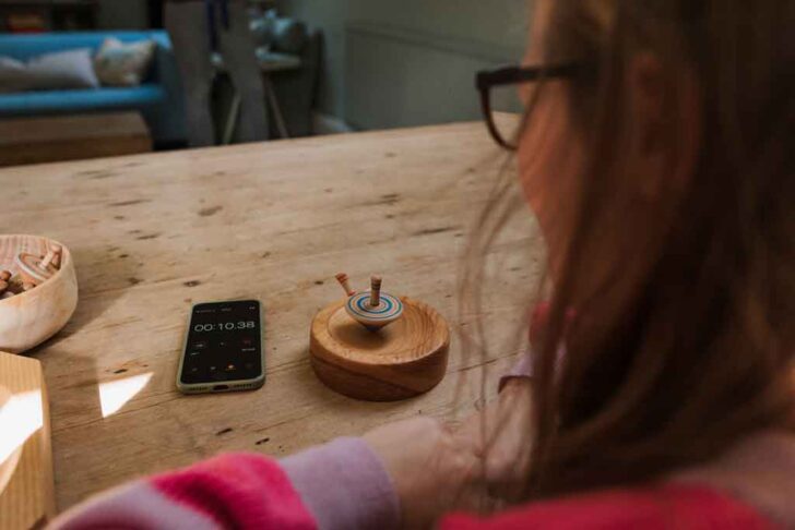 girl timing her spinning top spin with her phone timer.