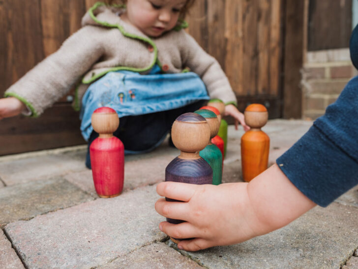 A young child engaged in imaginative play with various wooden toys scattered around on the floor