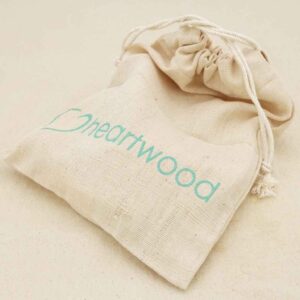 An nnbleached cotton drawstring bag with a heart symbol and the word heartwood printed on it in pale blue.