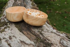 Two wooden bowls, one containing popcorn, sitting on a tree branch.