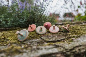 A group of colourful wooden spinning tops on a mossy stone wall in front of a lavender plant.