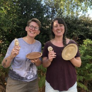 Two smiling women holding woodturned items including bowls and toadstools.