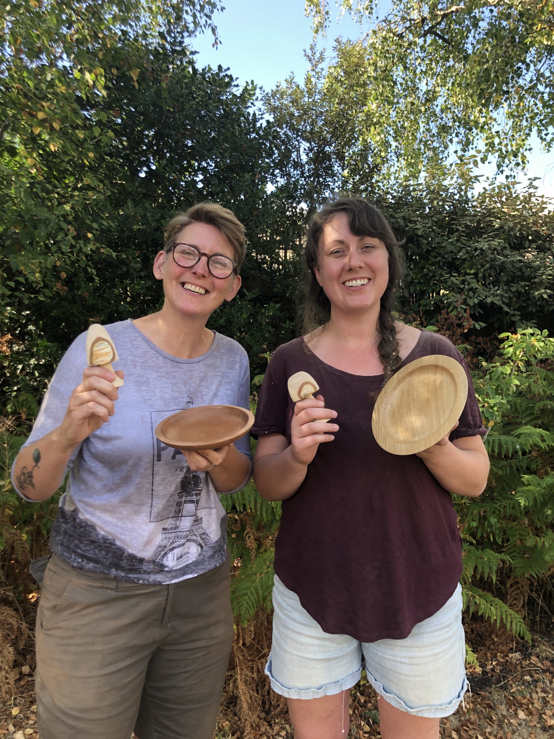 Two smiling women holding woodturned items including bowls and toadstools.