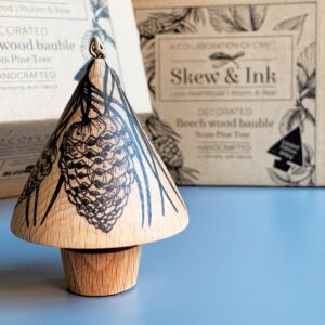 The Scots Pine wooden tree bauble in front of it's branded cardboard gift box.