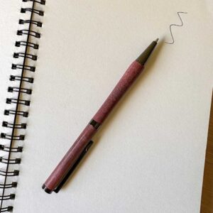 a wooden ballpoint pen writing in a spiral bound notebook