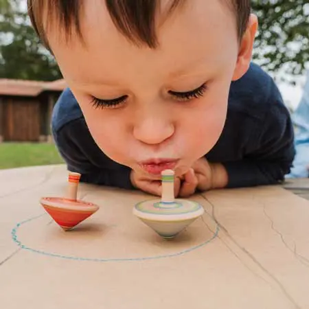 A young boy blowing gently on a colorful toy spinning top, watching it twirl and spin with delight