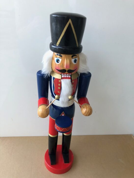 A wooden nutcracker wearing a red hat and a blue uniform, standing upright against a neutral background