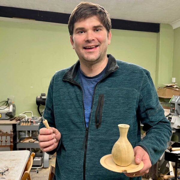 Smiling man holding a pen, vase and plate he turned on the lathe.