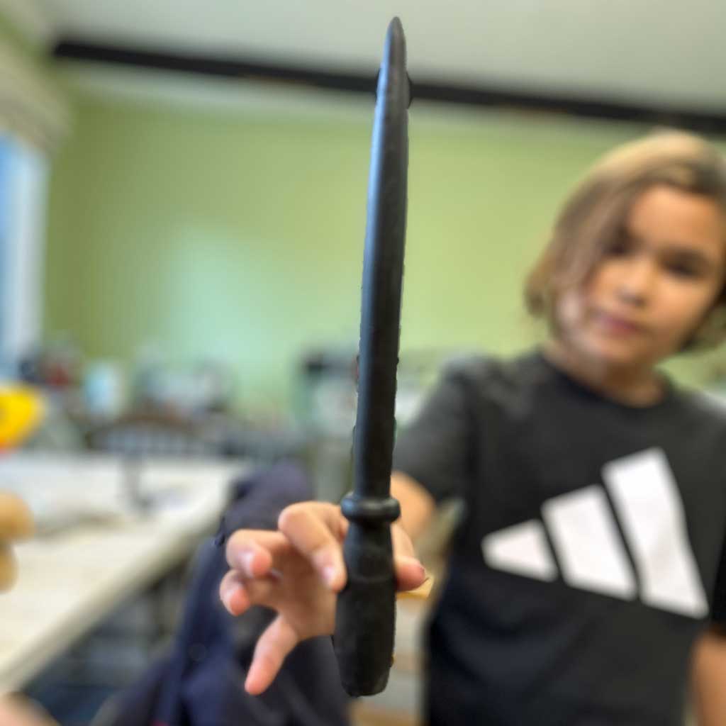 A young girl holding the wooden wand she turned on the lathe.