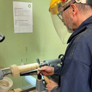 Student shaping a wooden table lamp on a woodturning lathe.