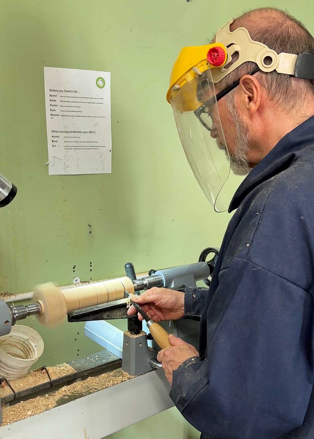 Student shaping a wooden table lamp on a woodturning lathe.